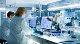 Zwei Wissenschaftler in weißen Laborkitteln arbeiten im Labor an Computern und Mikroskopen.