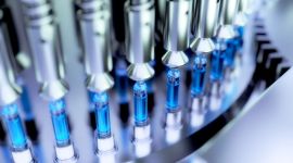 Nahaufnahme einer automatisierten Maschine, die Spritzen mit blauer Flüssigkeit befüllt.