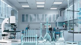 Mikroskop und verschiedene Labor-Glasgeräte mit Flüssigkeiten auf einem reflektierenden Tisch.